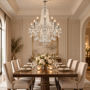 An ornate multi-tiered crystal chandelier hangs over a formal dining room with a dark wood table, white floral centerpiece, beige upholstered chairs, and elegant table settings.