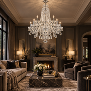 A large multi-tiered crystal chandelier with candle-style lights hangs in a luxurious, dark-toned living room with a fireplace, velvet armchairs, and a marble coffee table.