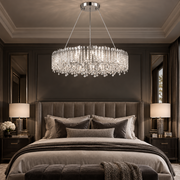 A luxury crystal chandelier with a circular frame and hanging teardrop pendants, suspended over a bed in a dark, elegant bedroom.